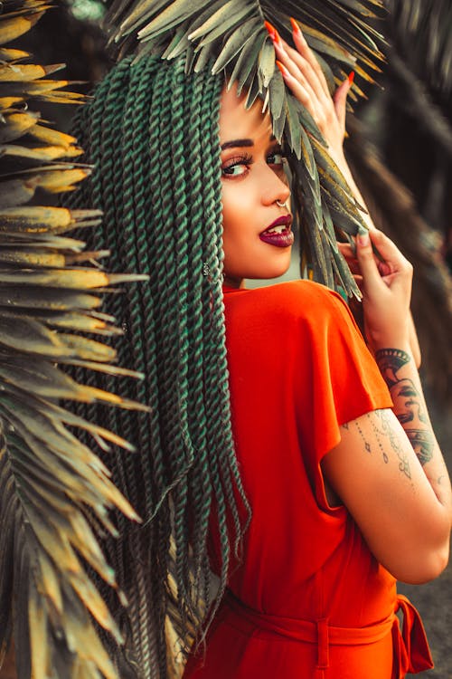 Shallow Focus Photo of Woman in Red Top Touching Leaves