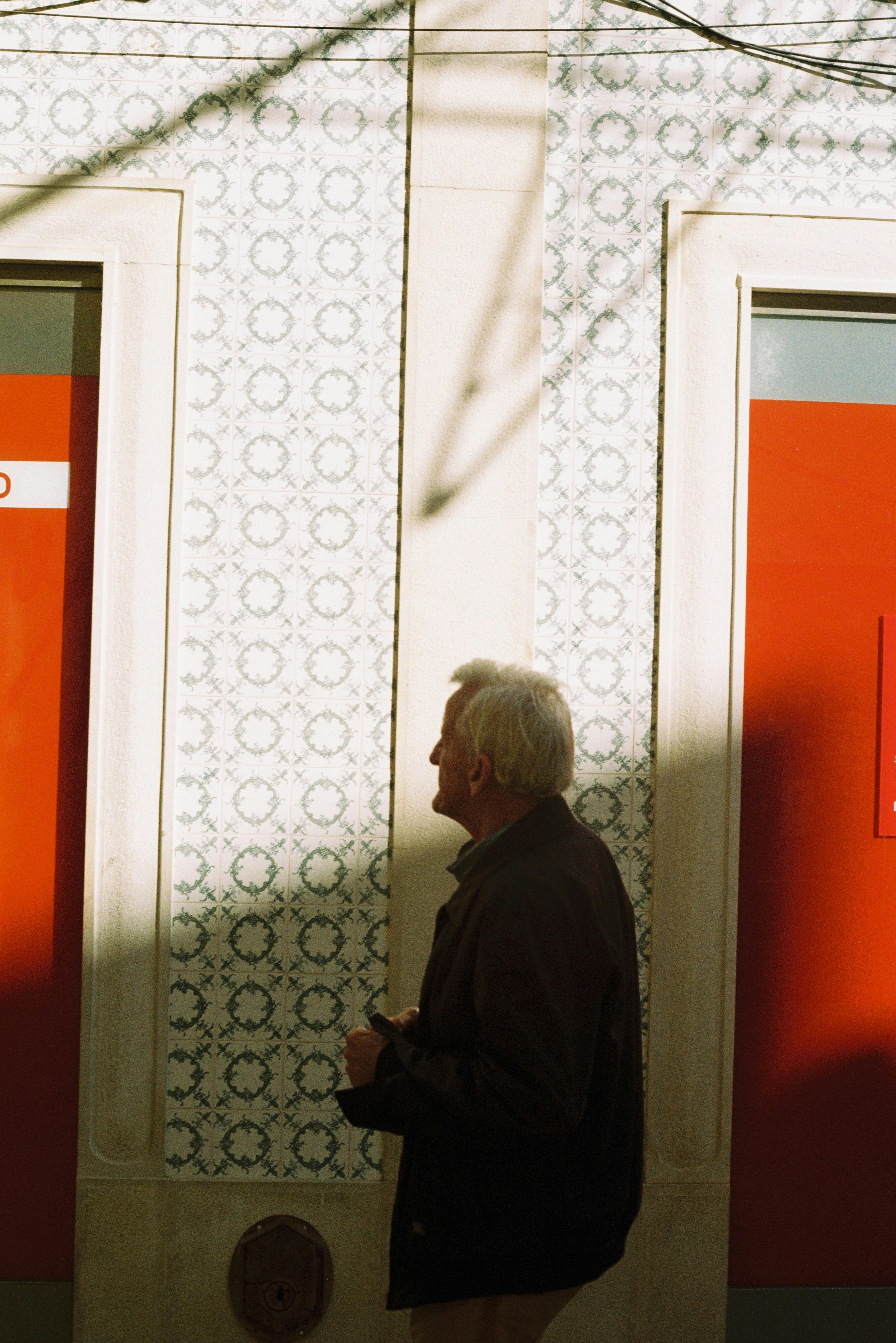 A senior man walks past a patterned wall with red accents in sunny Faro, Portugal.
