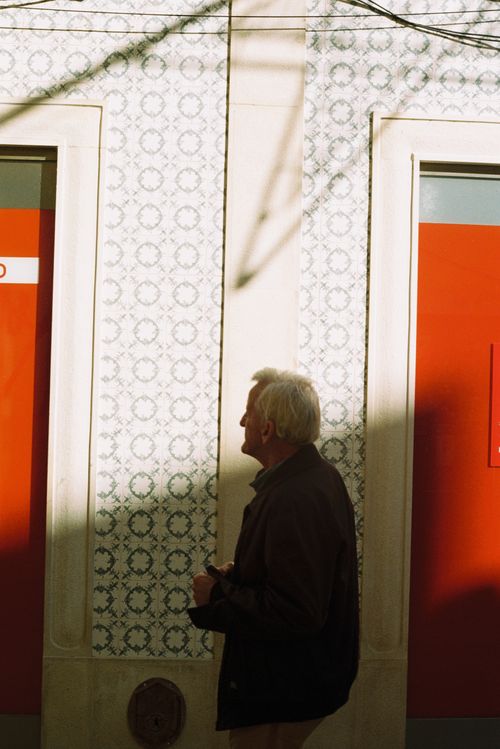 Free A senior man walks past a patterned wall with red accents in sunny Faro, Portugal. Stock Photo
