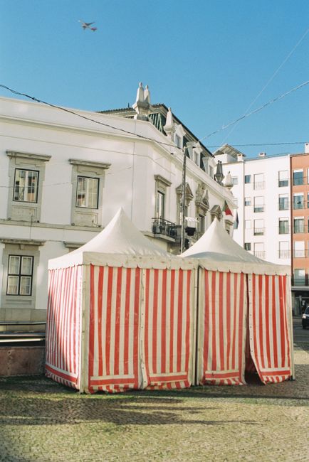 Red and white striped tents in a historic square in Faro, Algarve, under a clear blue sky.