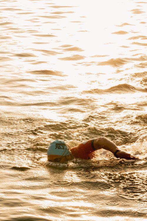 Free A triathlete swimming freestyle in open water during sunset, wearing a swim cap and goggles. Stock Photo