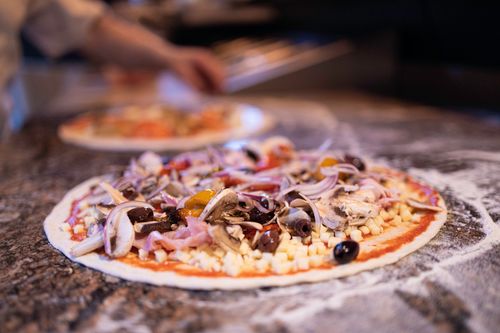 Free Delicious pizza topped with fresh vegetables and olives on a stone countertop. Stock Photo