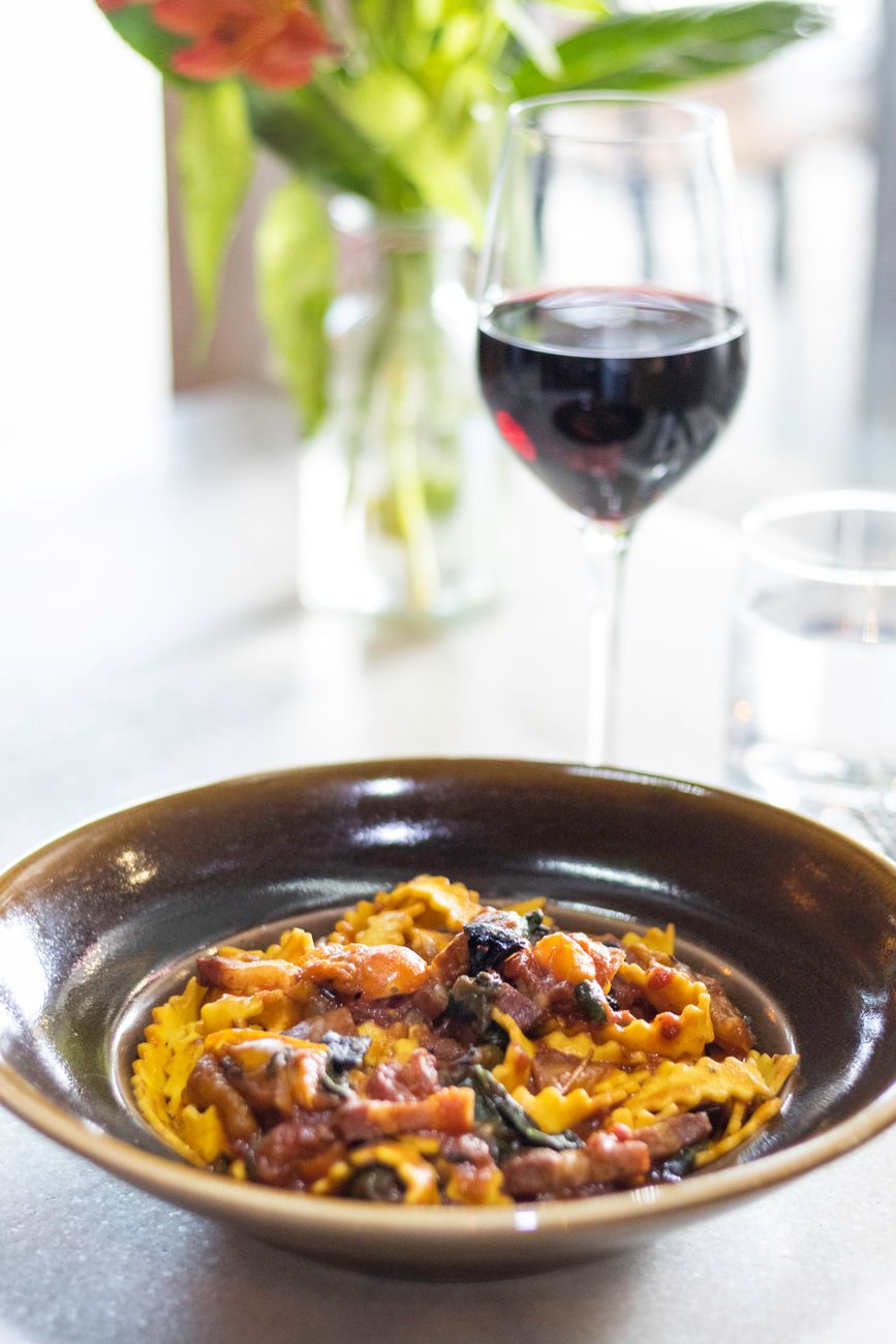 A plate of pasta beside a glass of red wine, echoing the family-table comfort these restaurants are selling.