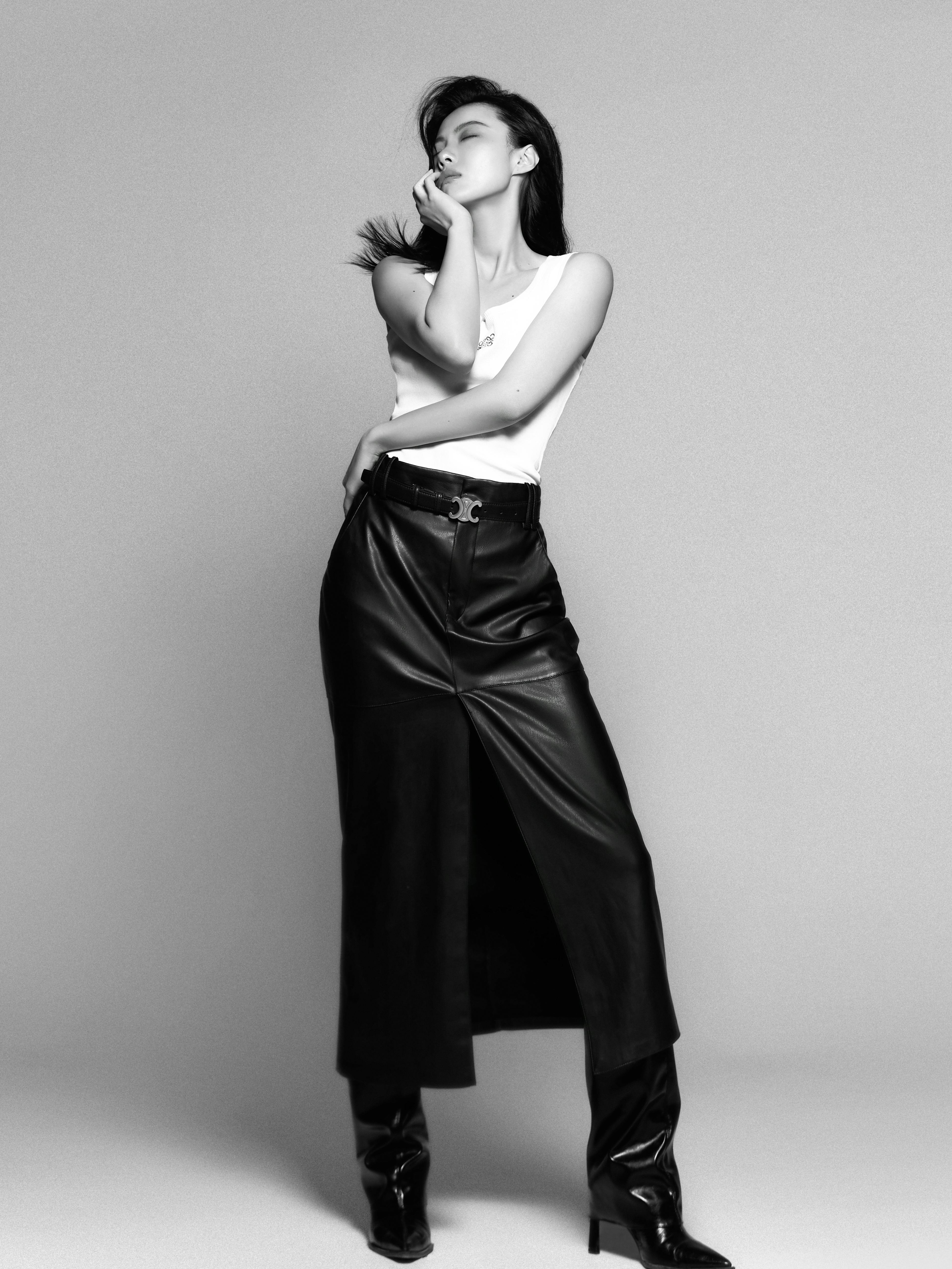 Elegant brunette woman posing in a black leather skirt in a studio setting.