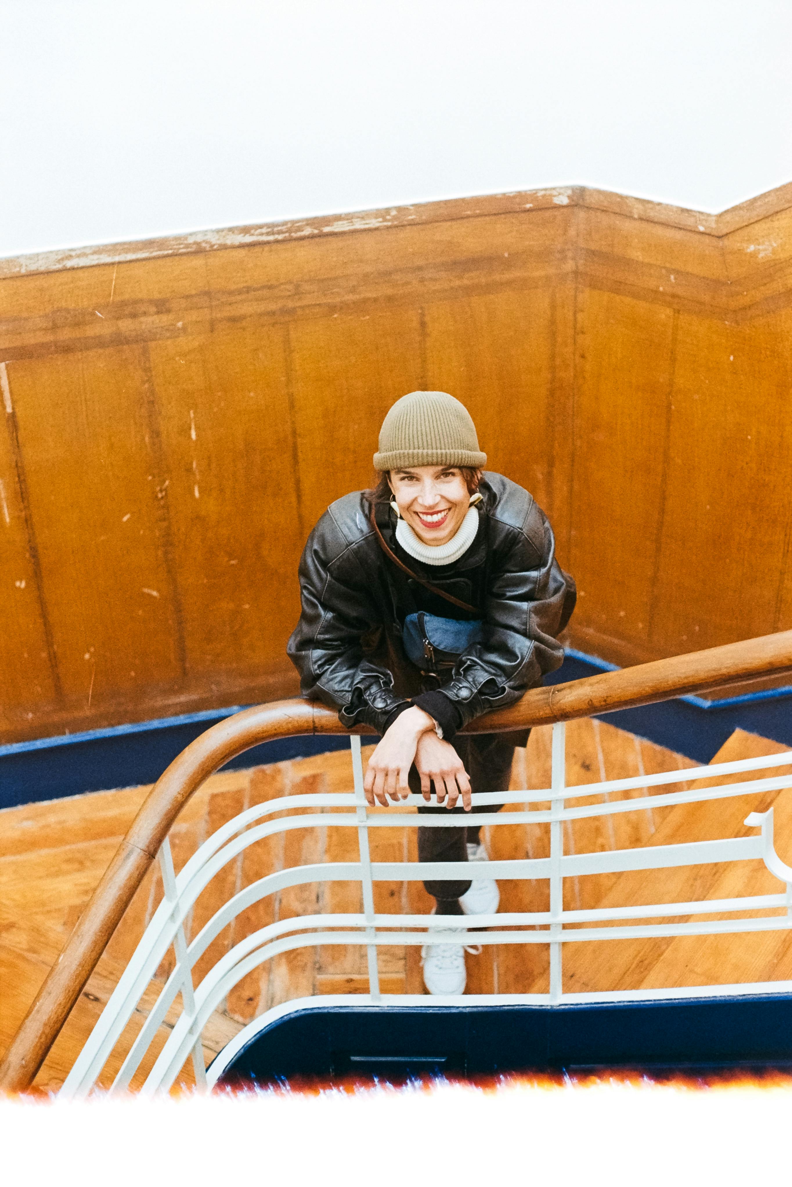 Fashionable woman with hat and jacket smiling on a wooden staircase in Lisbon.