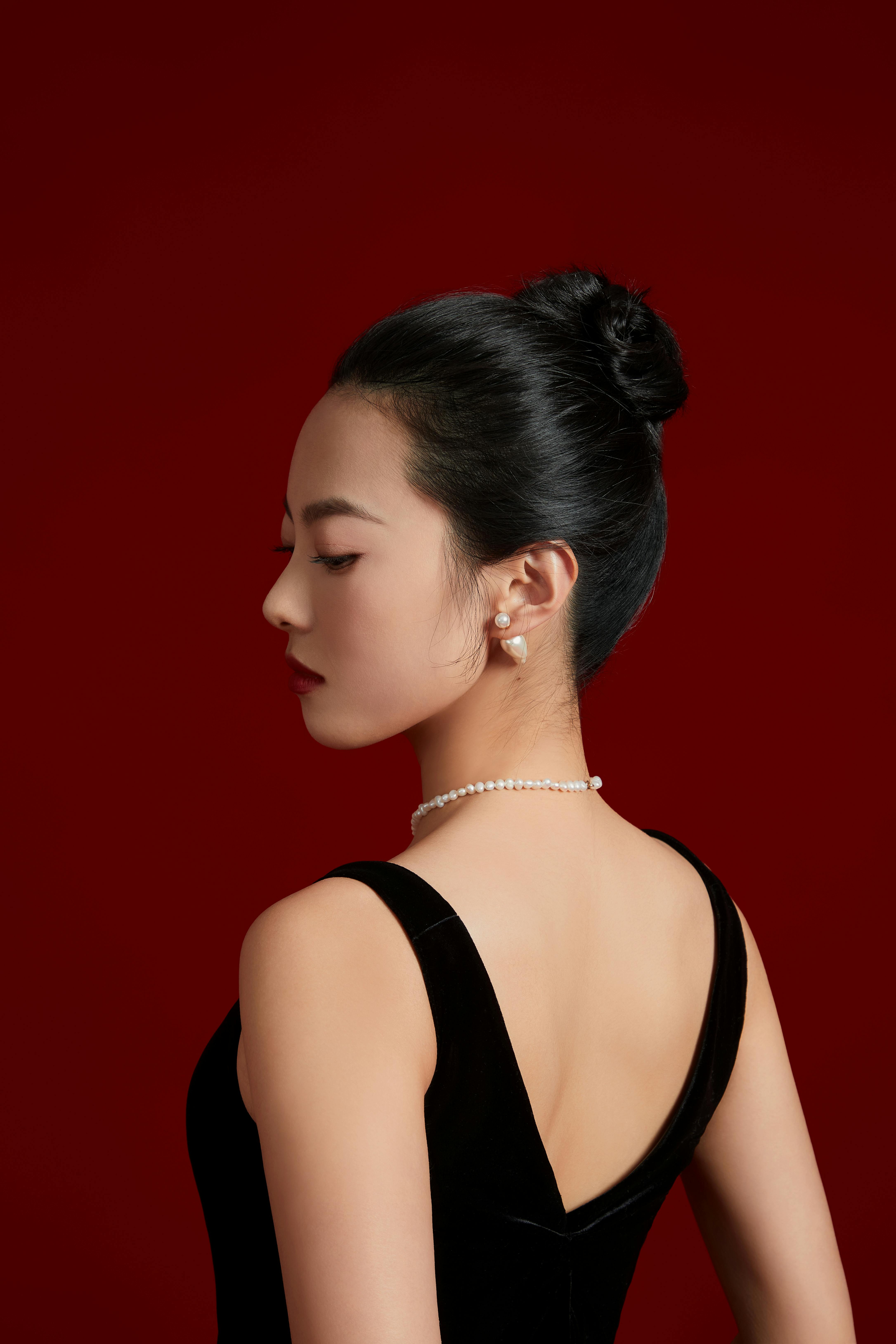 Sophisticated studio portrait of a woman posing in an elegant black dress against a red background.