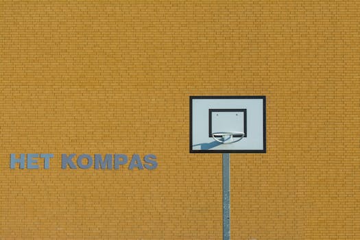 A basketball hoop against a yellow brick wall with the text 'HET KOMPAS' in an urban setting.