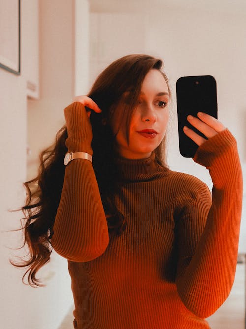 Woman Wearing Red Sweater Taking a Picture in a Mirror