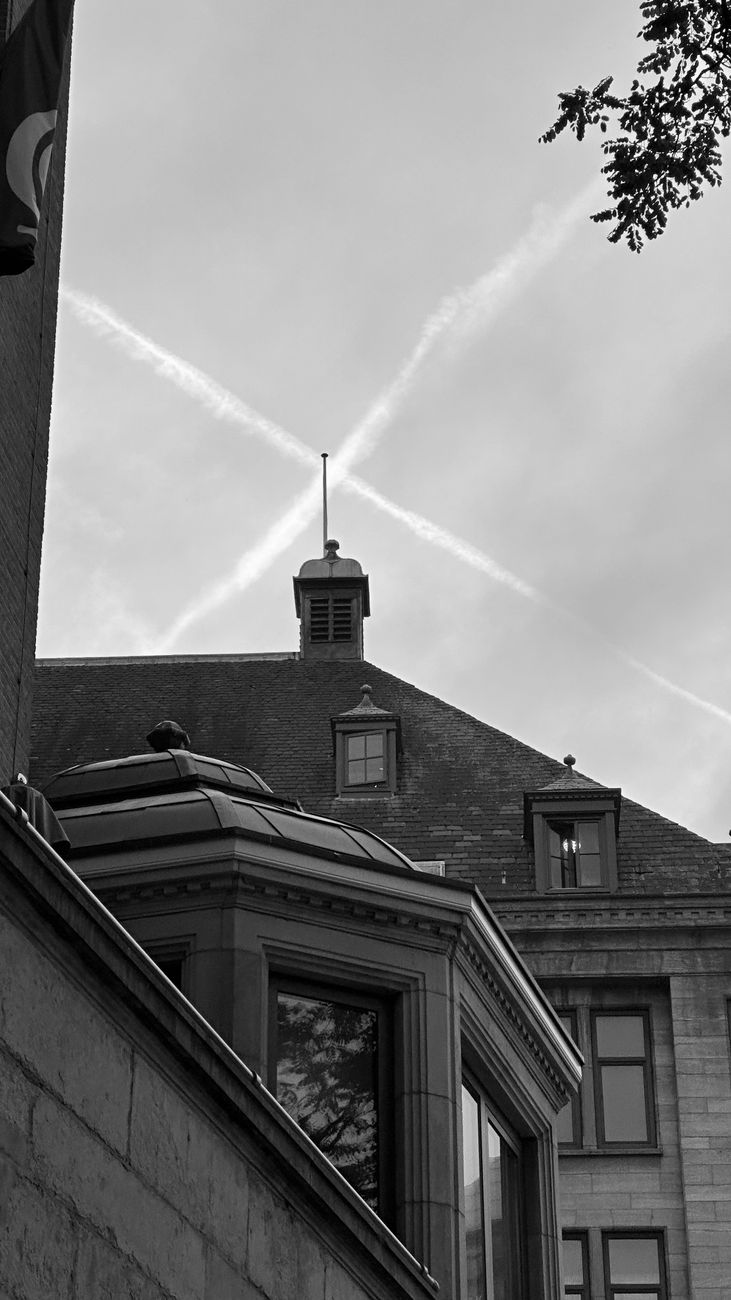 Zwart-witfoto van historische daken in Amsterdam met schoorstenen en bewolkte luchten.