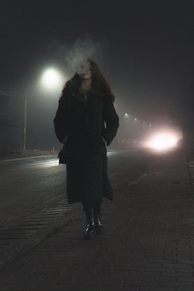 Woman In A Coat Walking On The Sidewalk At Night 