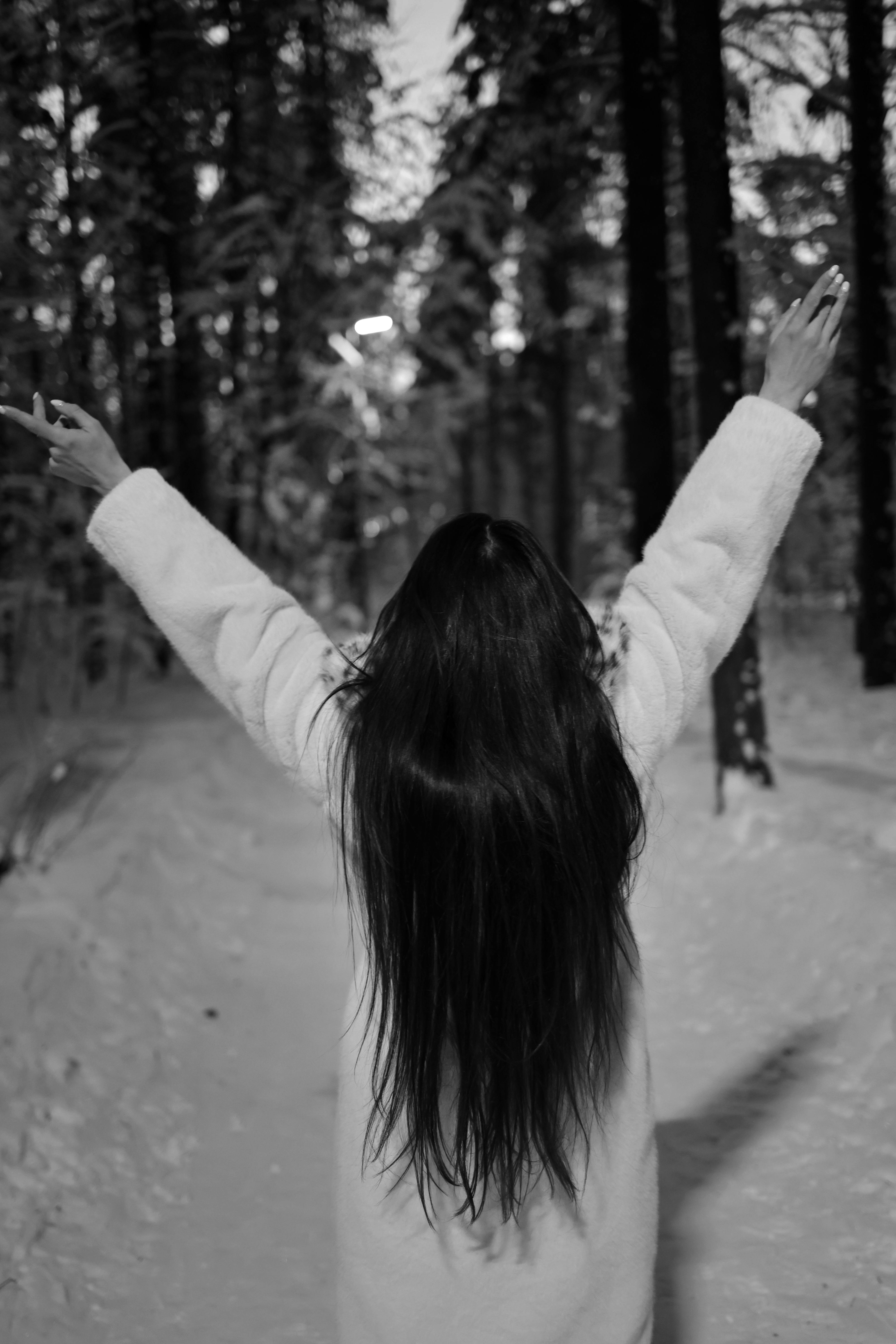 A brunette woman with arms spread stands in a snowy forest, embracing freedom.