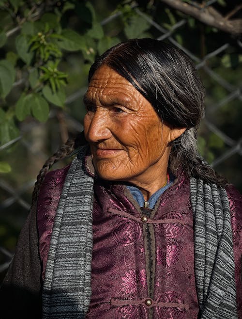 Photo of an Elderly Woman Sitting by the Fence 