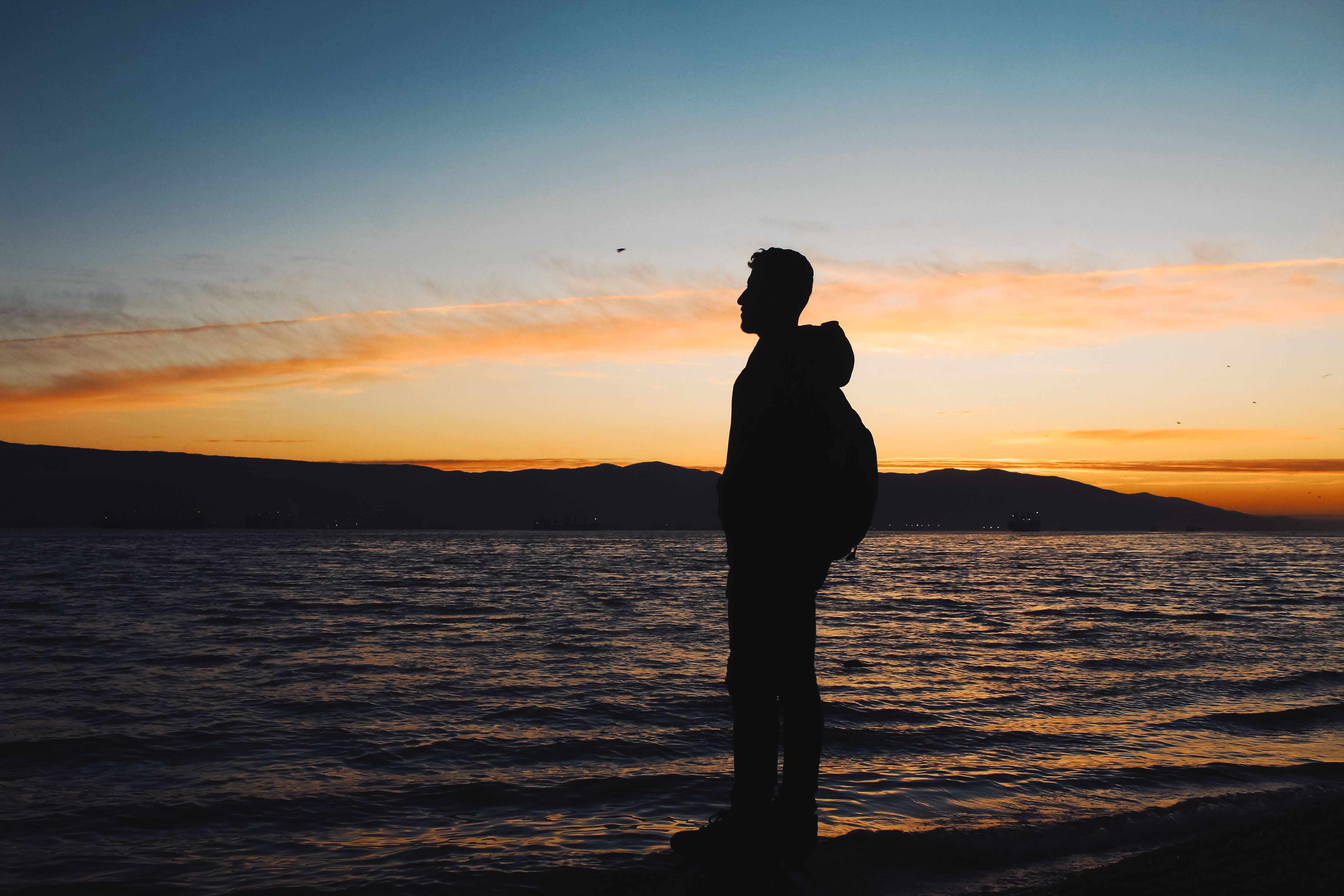 Silhouette of a Man Standing on a Shore at Sunset · Free Stock Photo