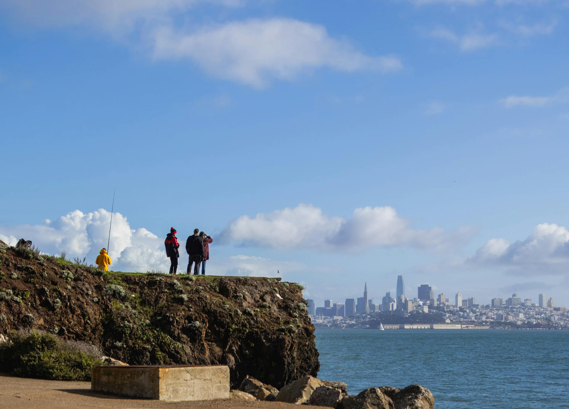 Tourists enjoying a view of San Francisco skyline from a rocky coast under a clear blue sky.