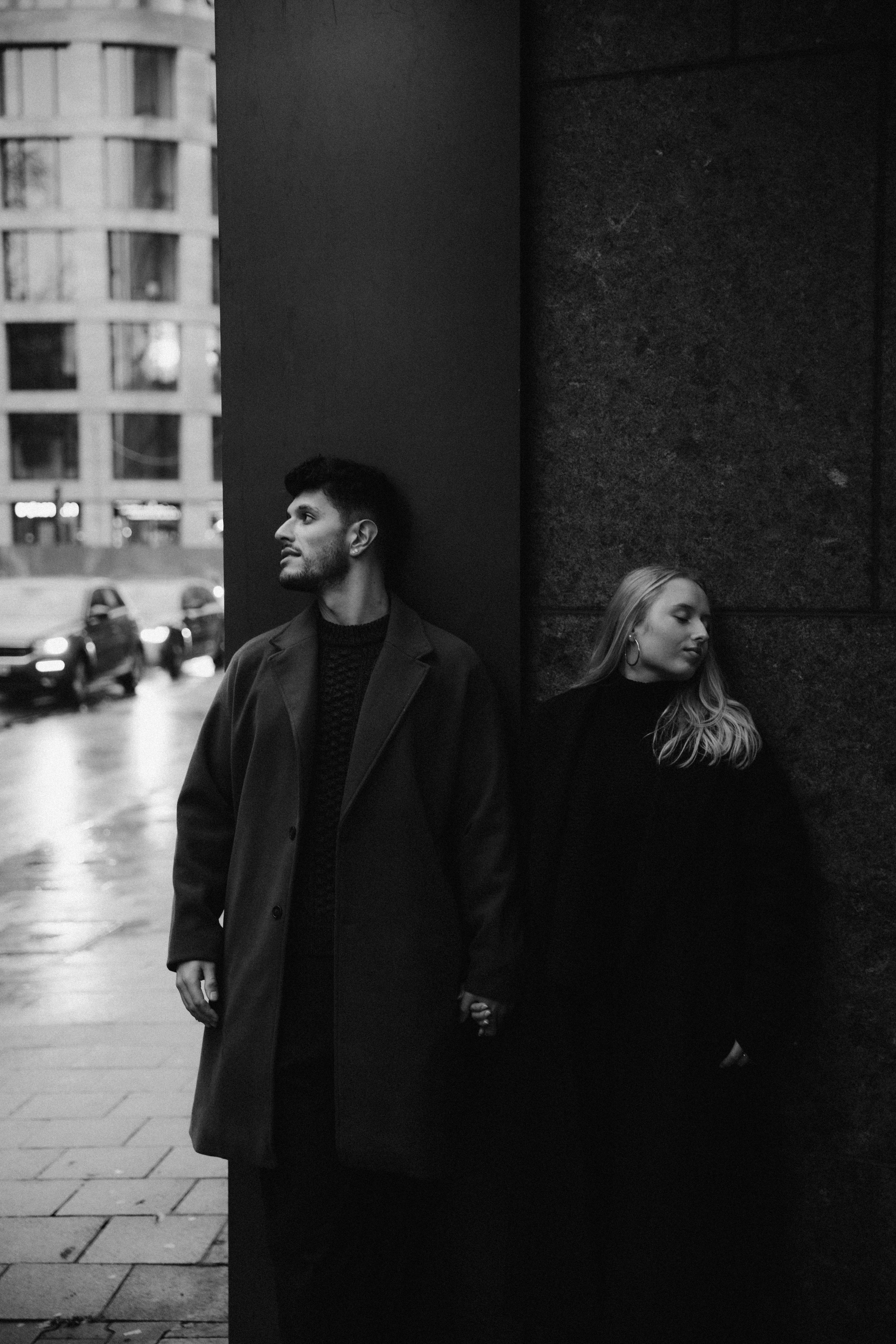 Black and white photo of a couple holding hands in a city on a rainy day, conveying love.