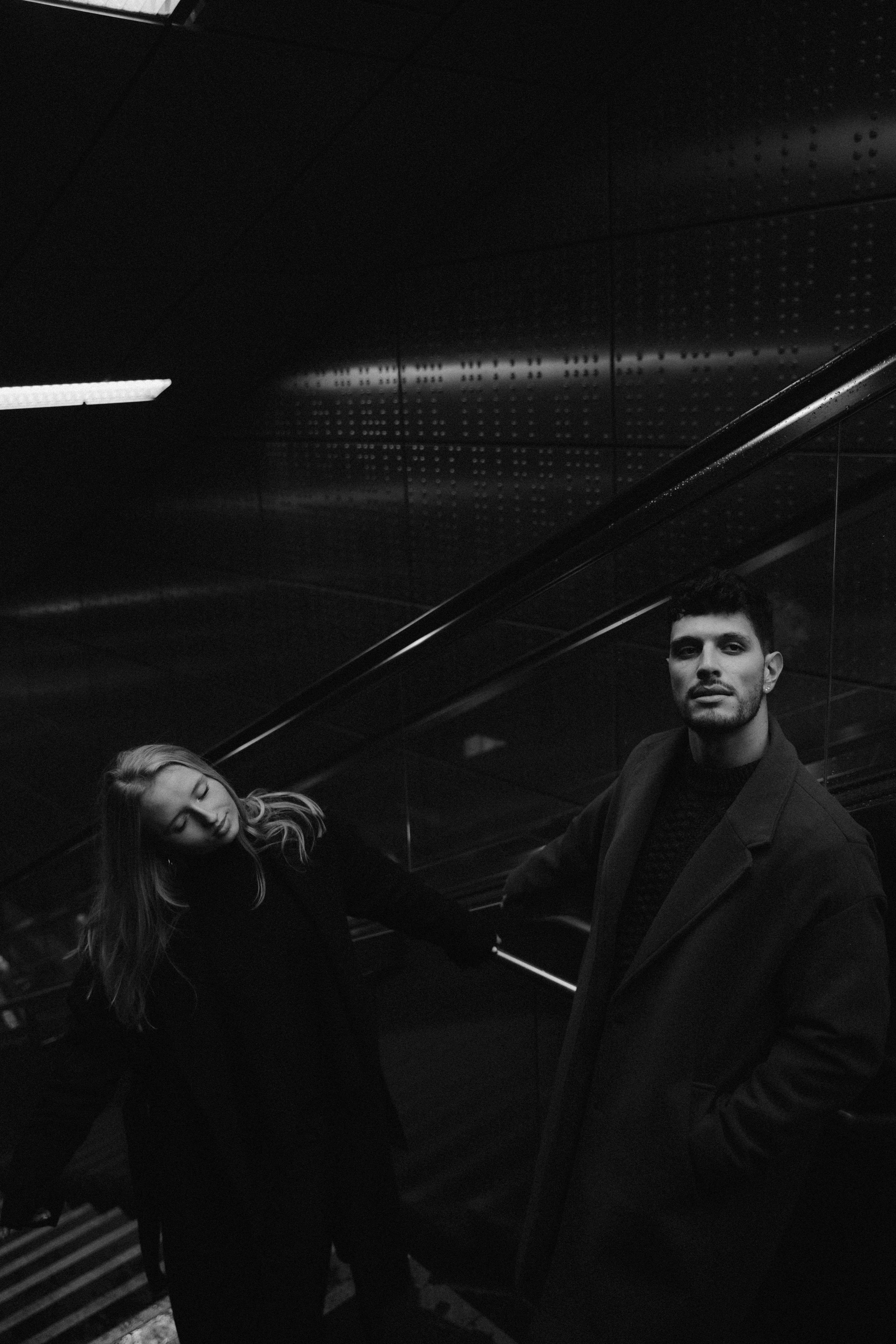 A fashionable couple poses on stairs in a dark urban environment in Düsseldorf, Germany.