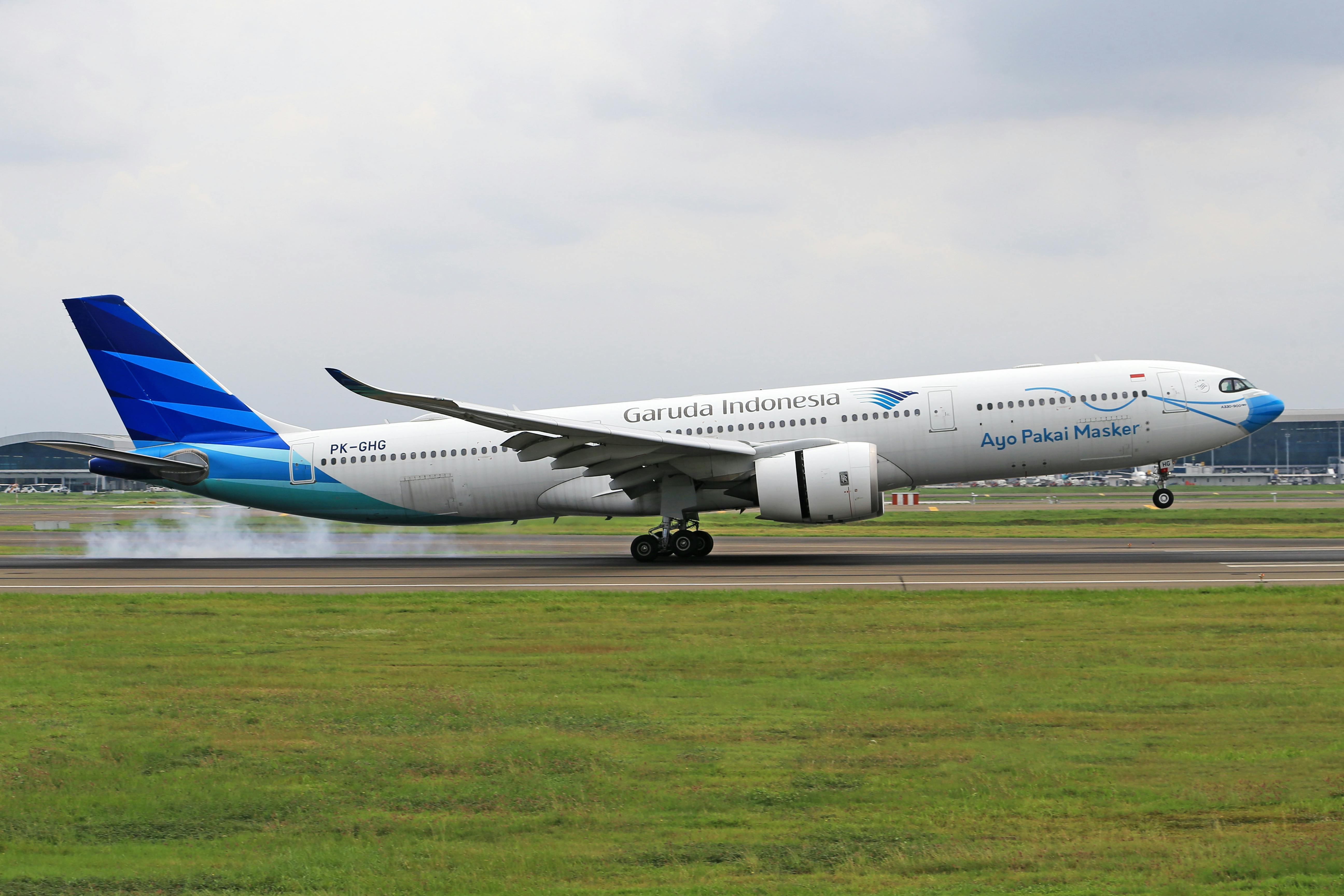 Garuda Indonesia airplane touches down on a runway amidst green fields.