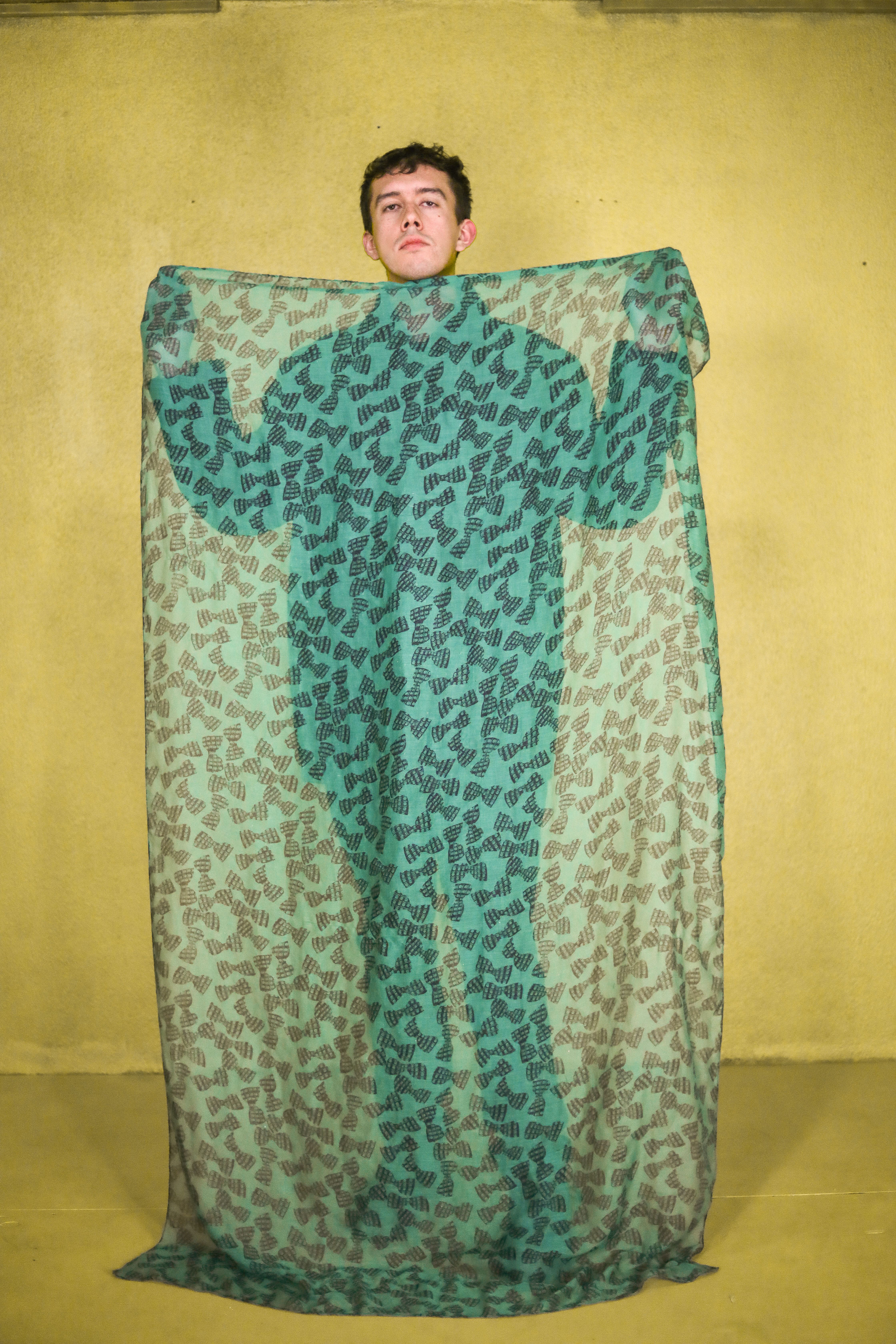 Creative studio portrait of a man posing with a green patterned scarf against a yellow background.