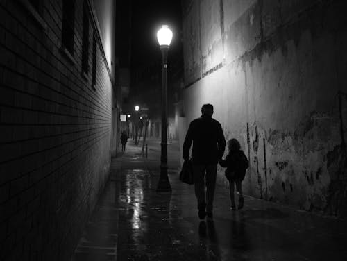 Grandfather Leading His Little Granddaughter by the Hand Down an Alley on a Rainy Evening