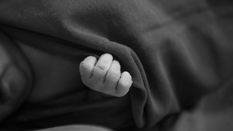 Close-up of a newborn baby's hand wrapped in a soft blanket, black and white tones.