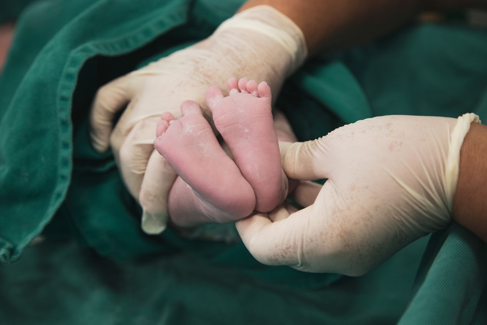 A midwife wearing gloves supporting a newborn baby during care