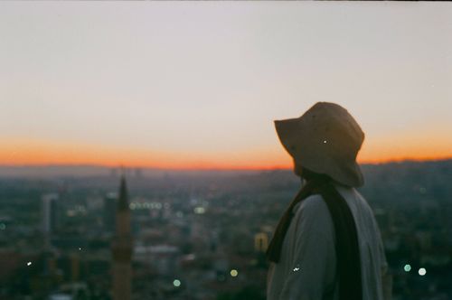Free A captivating view of a person in a hat overlooking a city at sunset, evoking travel and exploration. Stock Photo