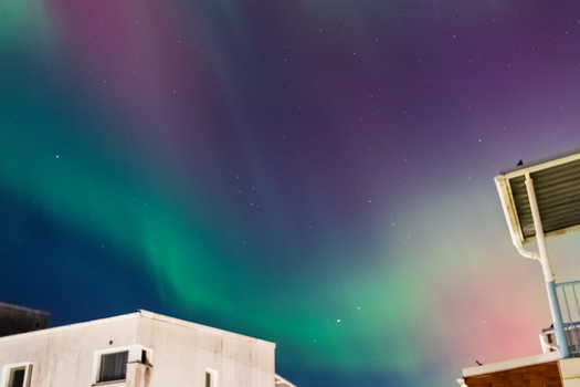 Capture of Northern Lights in vibrant green and purple over Tampere, Finland's cityscape at night.