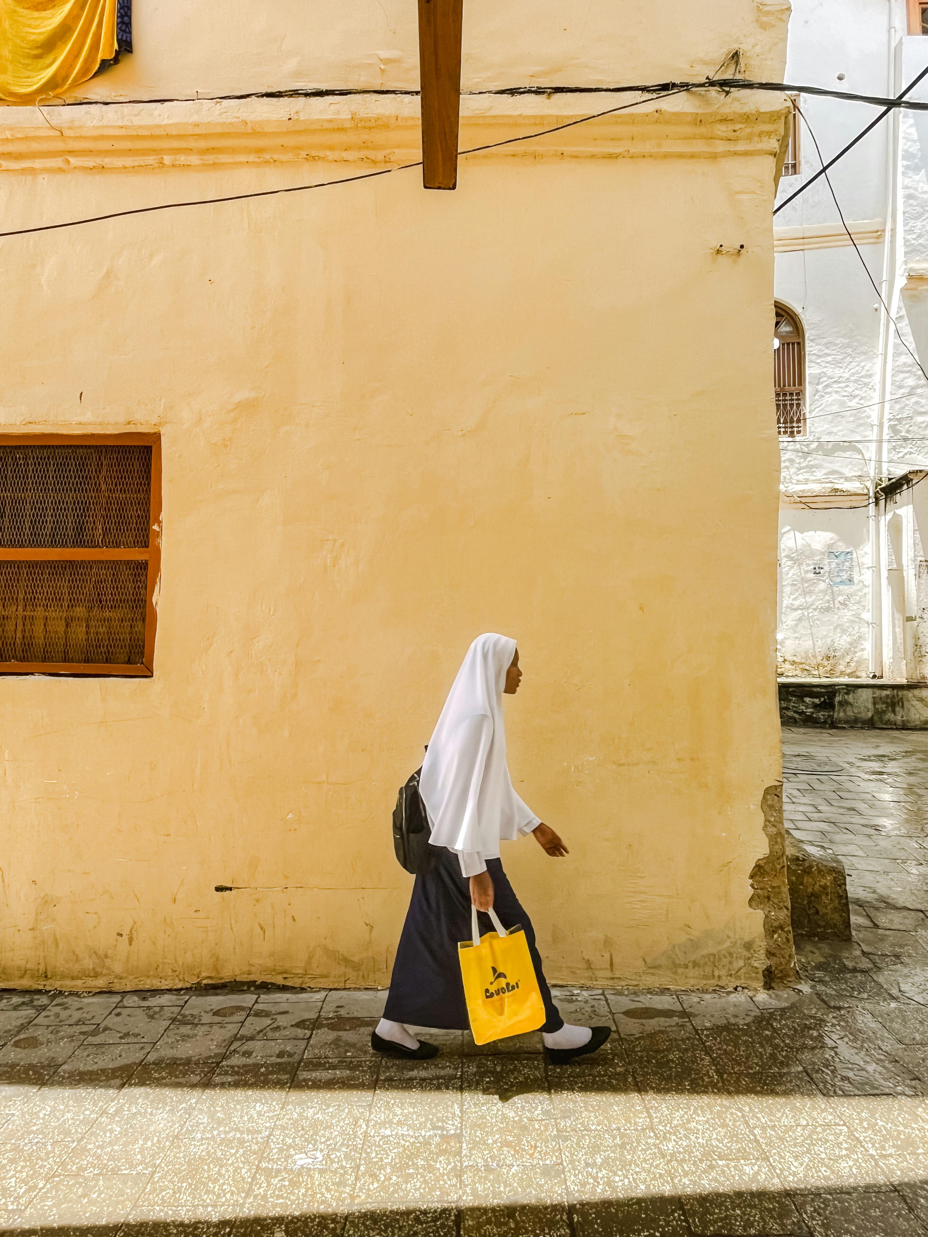 A woman in a hijab walks on a sunny street in Zanzibar, Tanzania, showcasing the vibrant urban life.