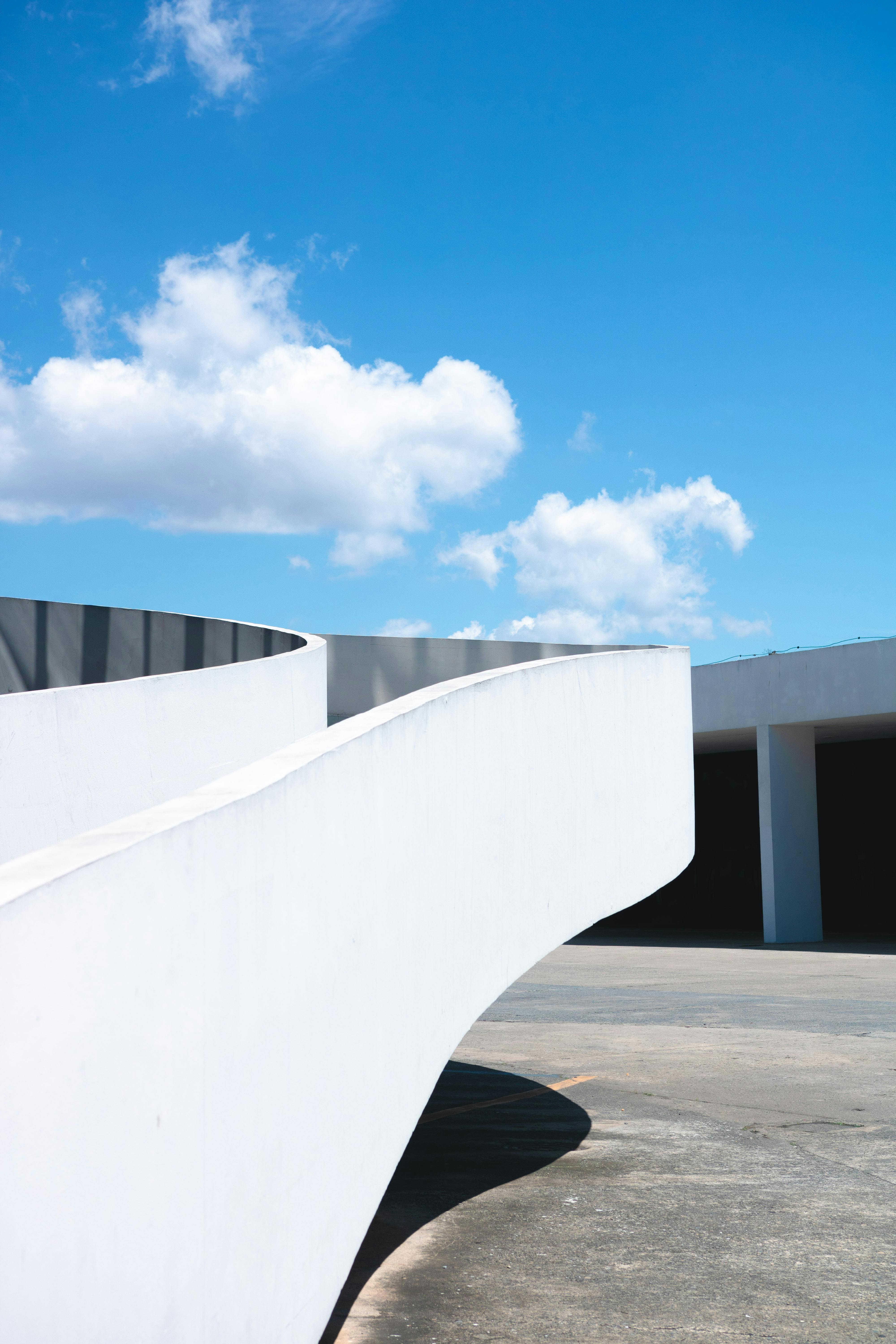 一座采用弧形设计的极简主义现代建筑，映衬着明亮的蓝天和云层