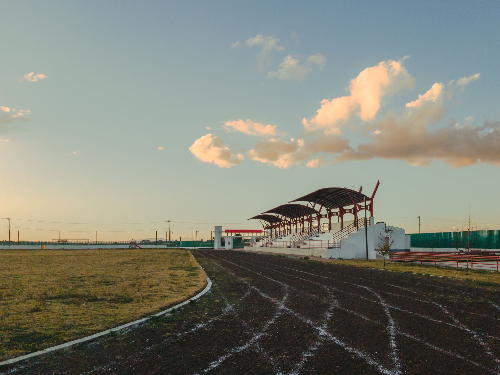 A traditional cockfighting arena at dusk, empty wooden stands, officials inspecting the ring under warm lights