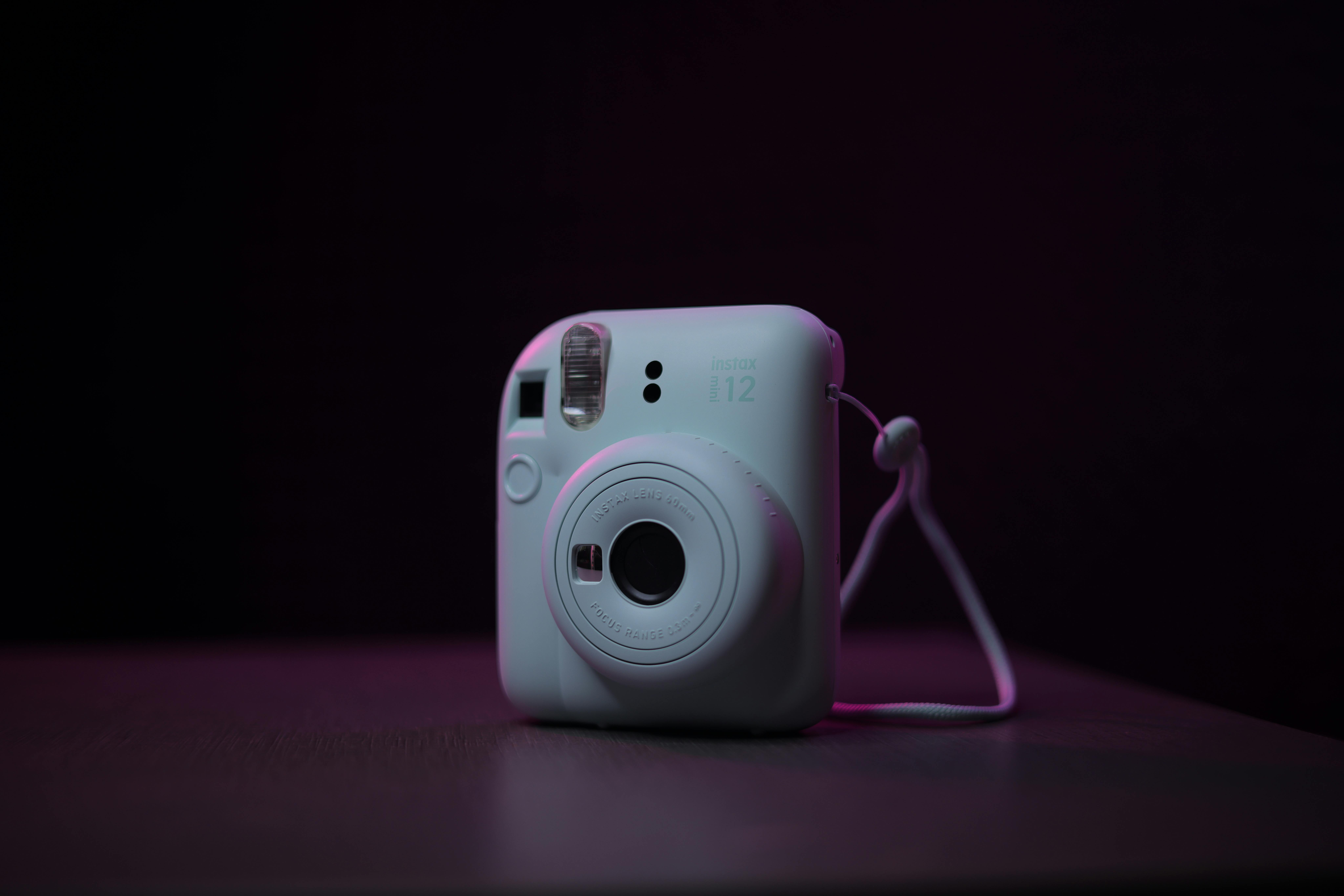 Close-up of a Fujifilm Instax Mini 12 instant camera in a minimalist, dark setting.