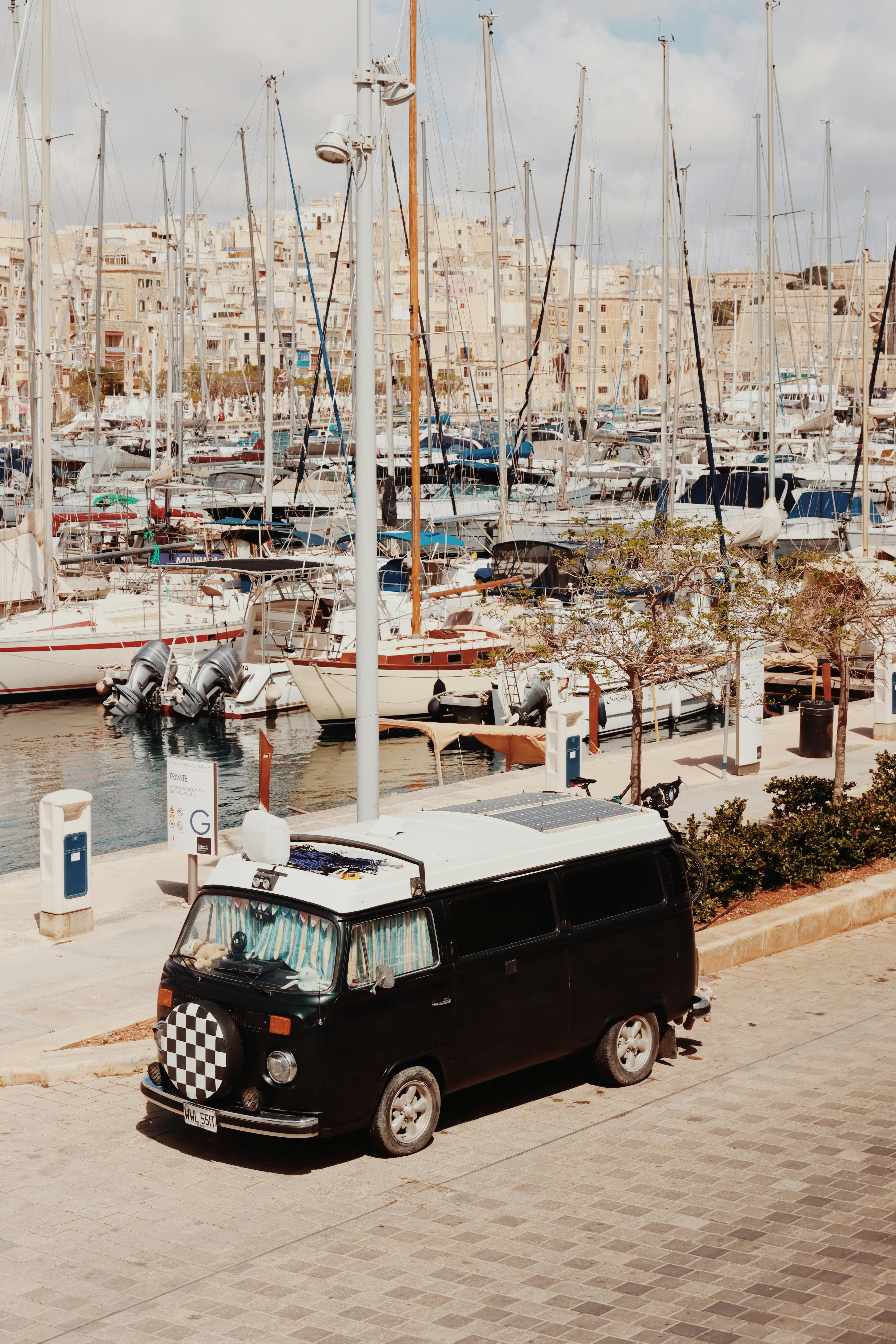 A vintage Volkswagen van parked by the harbor in Valletta, Malta, with boats in the background.