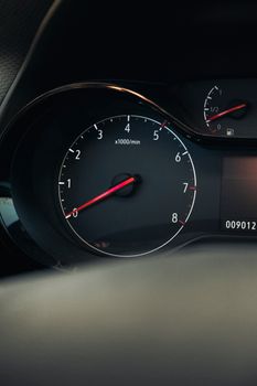 Detailed view of a car's tachometer showing numbers and red needle in focus.