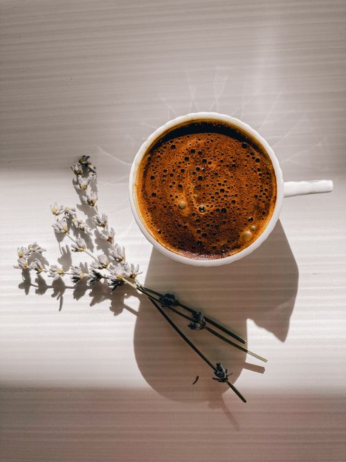 Free Top-down view of a coffee cup paired with lavender on a sunlit table. Stock Photo