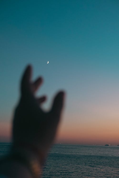 Blurred Hand against an Evening Sky with the Moon