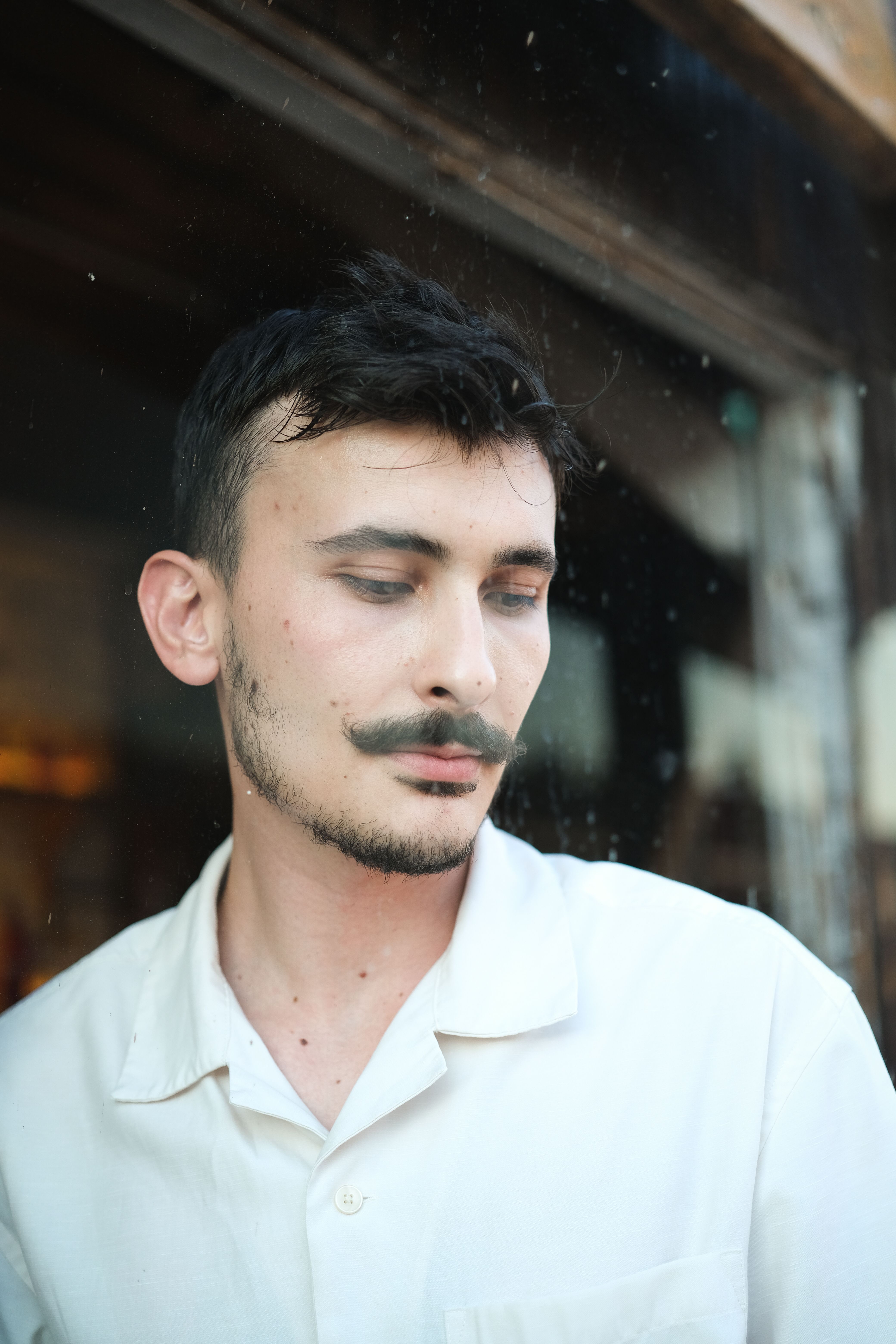 Close-up of a caucasian man with a mustache looking pensive. Wearing a white shirt outdoors.