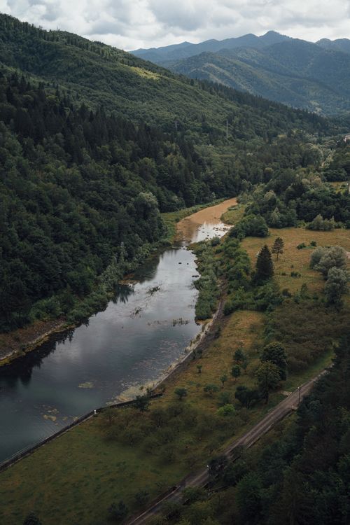 Free A breathtaking aerial shot showcasing a river winding through lush green mountains and forests. Stock Photo