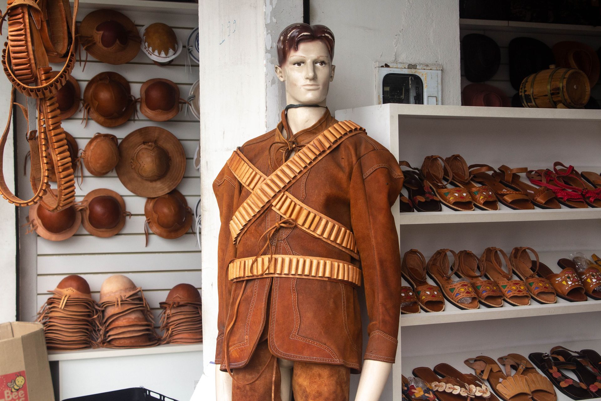 A mannequin dressed in traditional leather attire surrounded by leather goods and hats in a shop display.