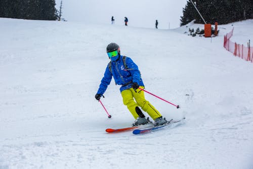 Photo of a Skier Wearing a Blue Ski Jacket and Yellow Trousers on a Ski Slope