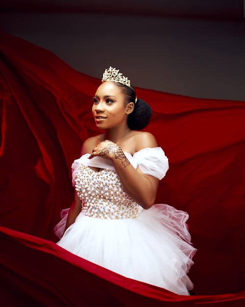 Woman Wearing a White Tulle Dress and a Tiara, Standing against a Red Fabric