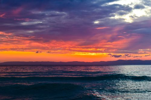 Free Vibrant sunrise casting colorful hues over the ocean with dramatic clouds. Stock Photo