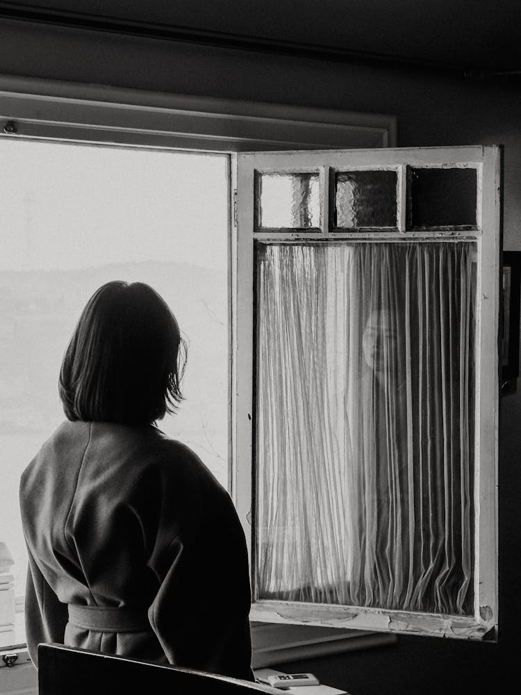 Black And White Photo Of A Woman Standing By A Window