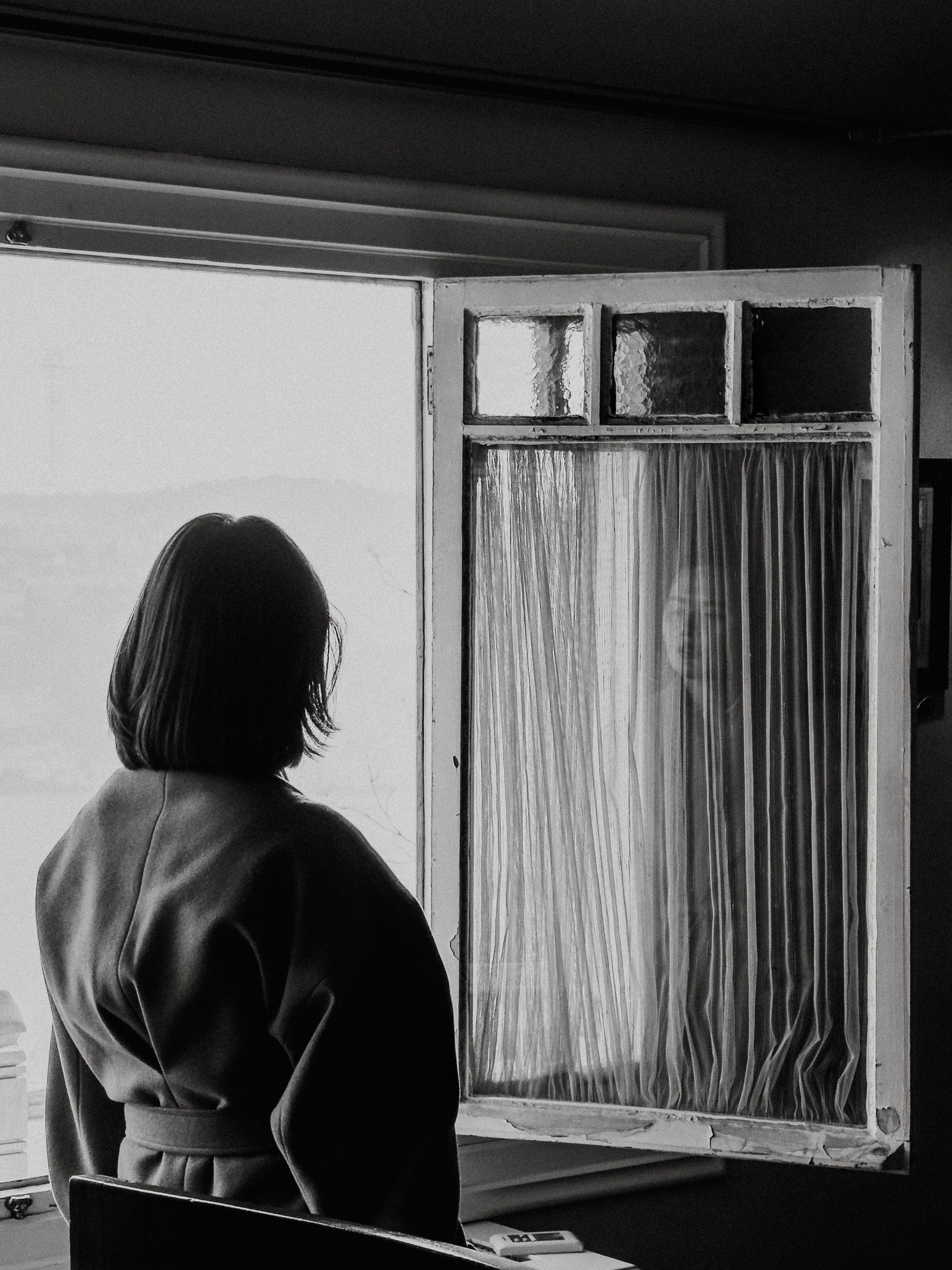 Black and White Photo of a Woman Standing by a Window · Free Stock Photo