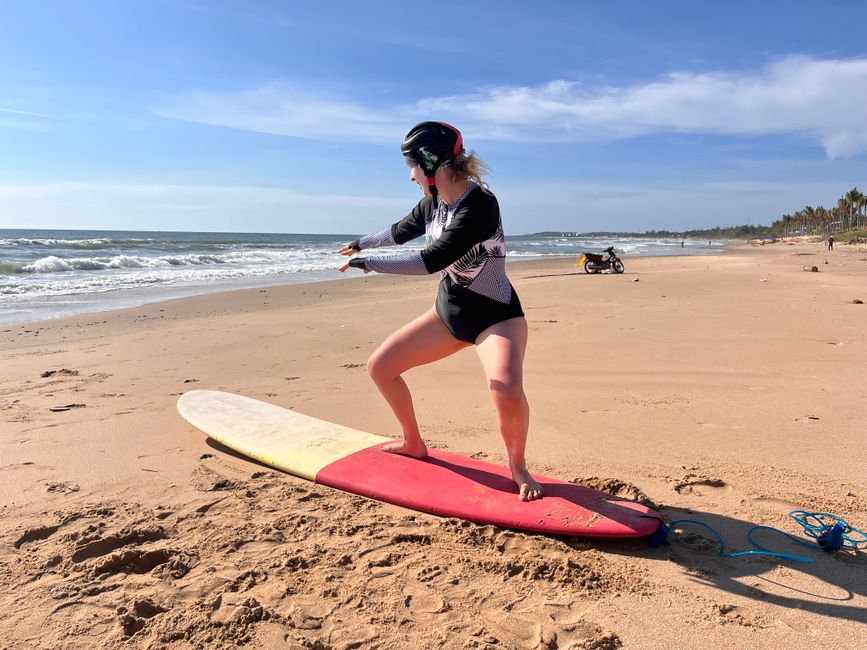 A woman stands on a surfboard practicing her stance on a sunny beach day.
