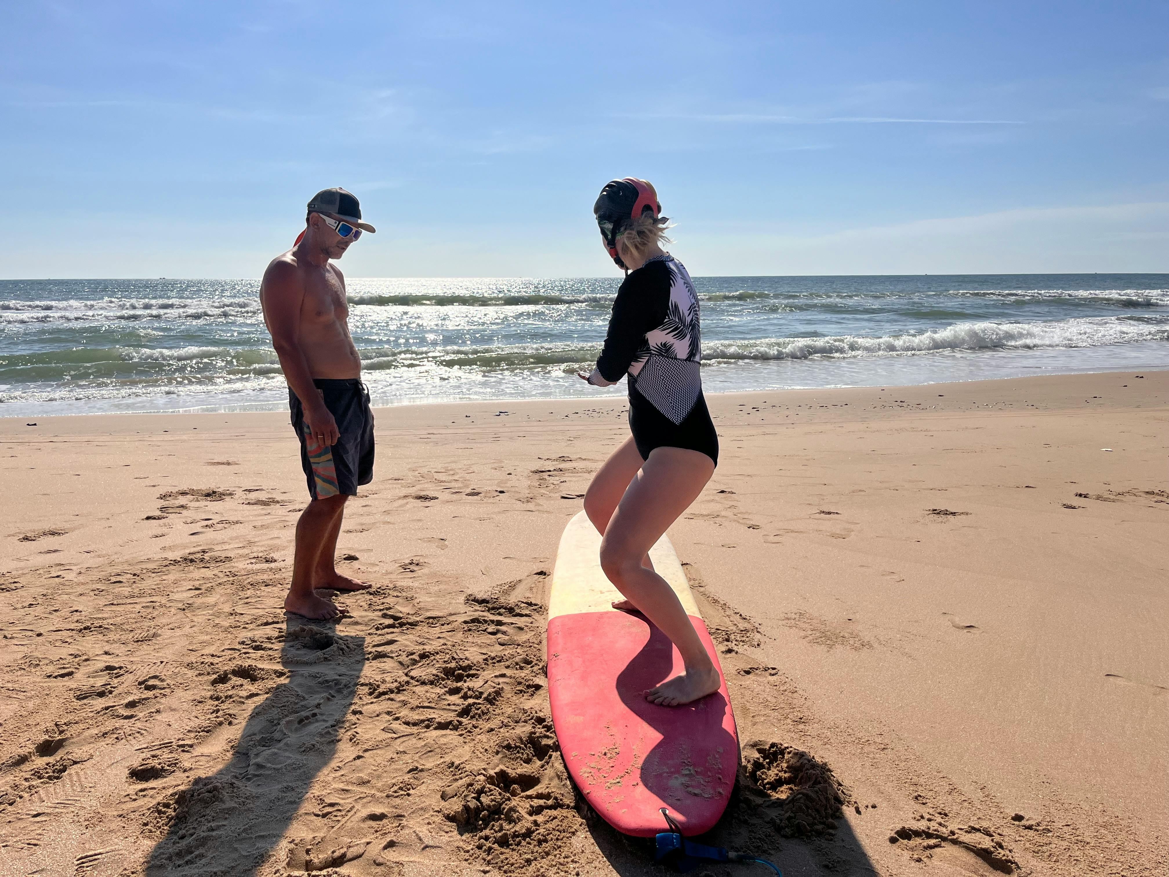 A woman learning to surf with an instructor on a sunny beach day.