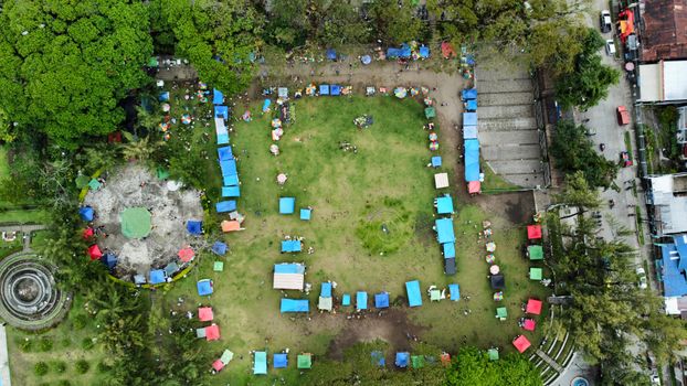 A vibrant aerial shot of a lively outdoor market festival with colorful stalls and green surroundings.