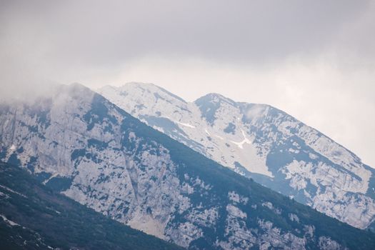 Misty mountain peaks with rocky surfaces under cloudy skies, creating a dramatic landscape.