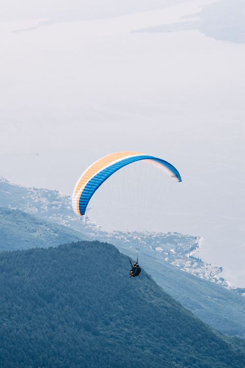 Free Experience the thrill of solo paragliding above a coastal landscape with breathtaking views. Stock Photo