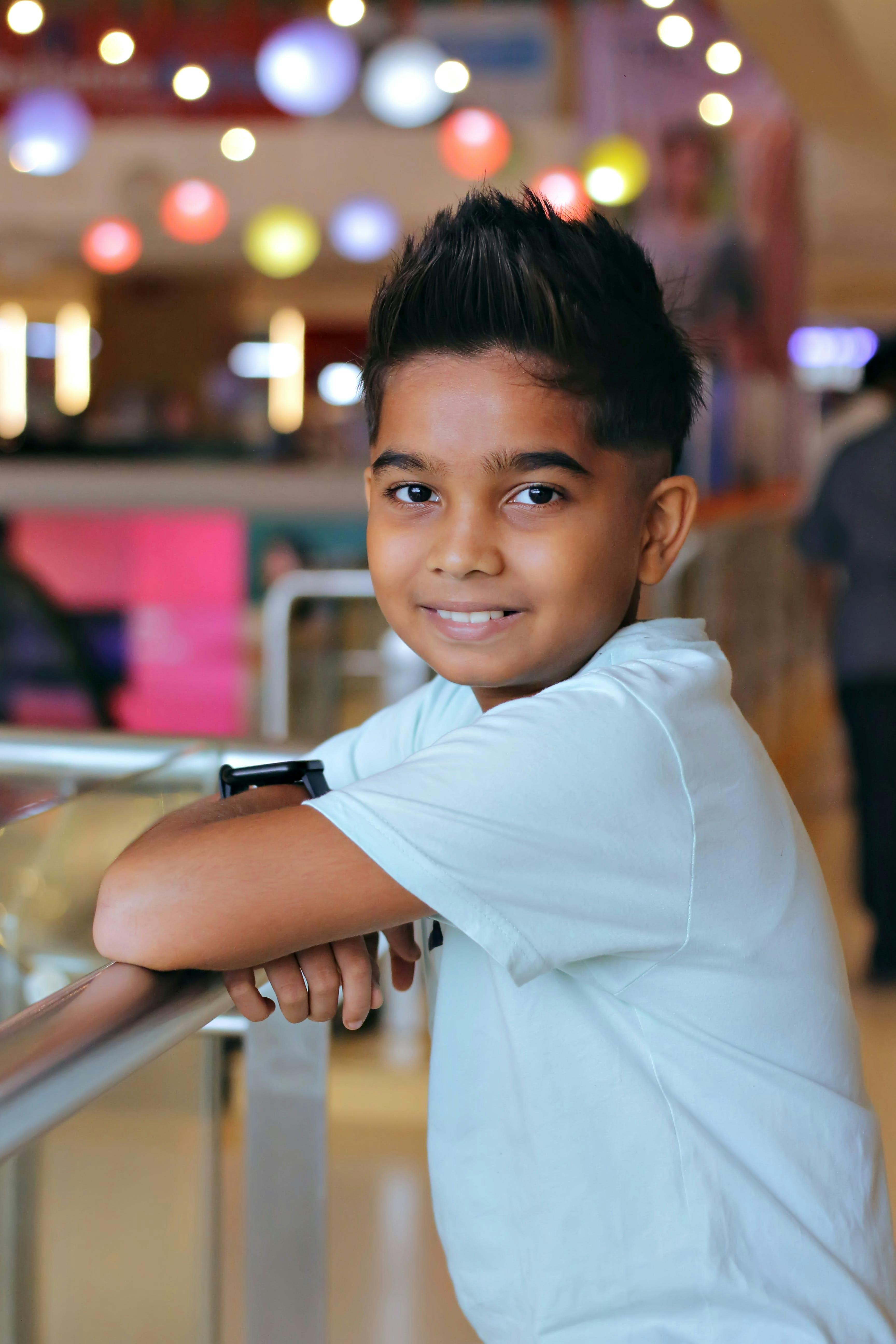Portrait of a young boy smiling indoors with colorful lights in the background.