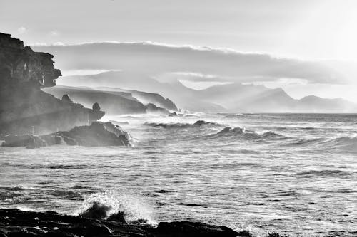 Black and White Photo of Waves Breaking on a Rocky Shore 